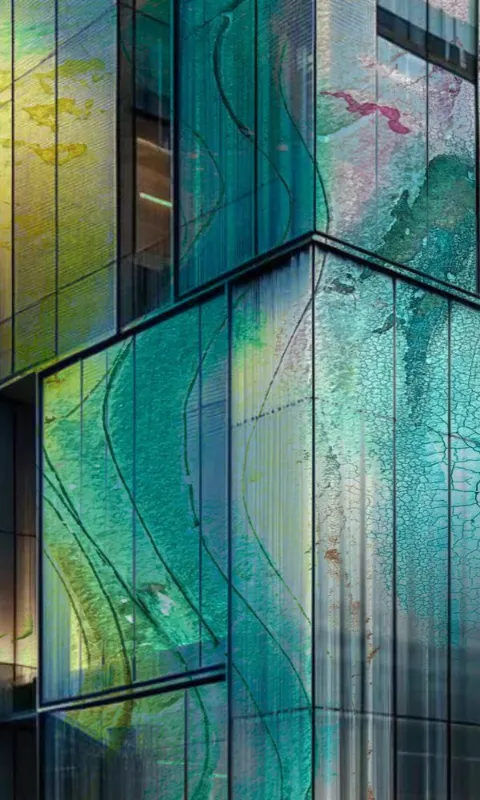 A tall glass tower in teal and amber reflections, built from overlapping panes