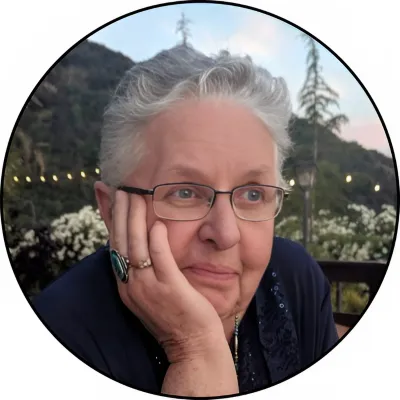 Ruth M Bass, smiling softly with her chin resting on her hand, flowers and string lights behind her